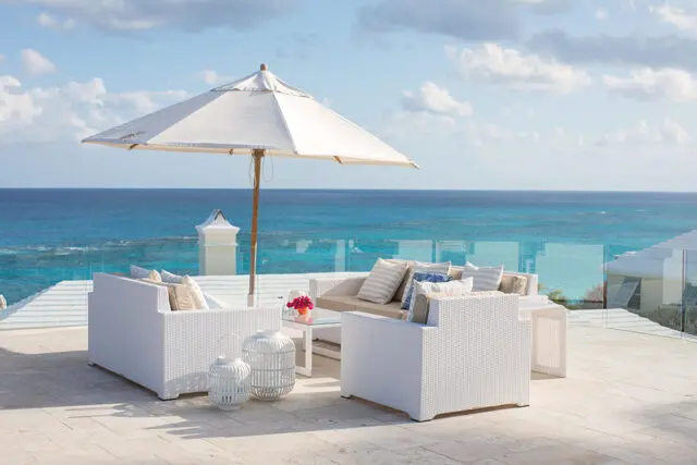 White wicker patio furniture with cushions and umbrella overlooking the ocean.