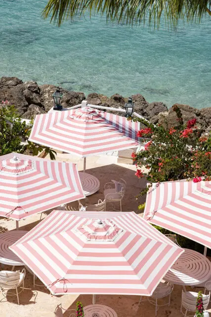 Pink and white striped umbrellas over white patio tables and chairs by the ocean