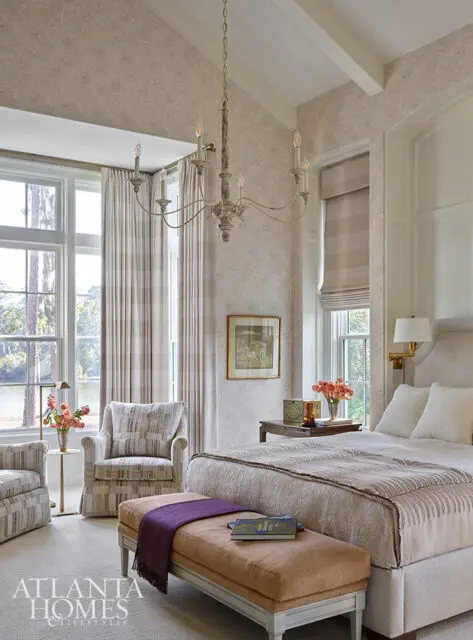 Bedroom with patterned wallpaper, vaulted ceiling, chandelier, and upholstered furniture.