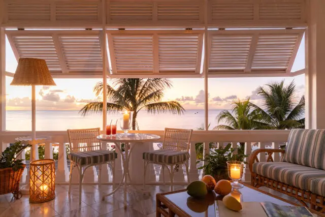 Balcony with wicker furniture, drinks, and ocean view at sunset