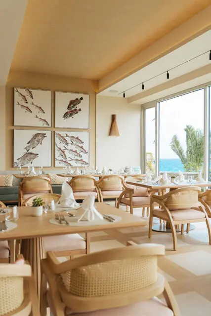 Restaurant dining room with light wood furniture, cane-backed chairs, and artwork of fish on the