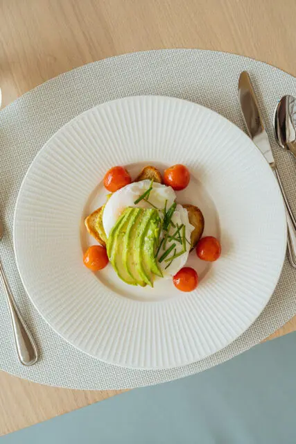 Poached egg with sliced avocado, cherry tomatoes, and toast on a white plate
