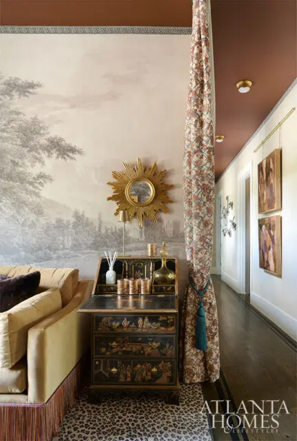 Living room with chinoiserie desk, sunburst mirror, and landscape wallpaper