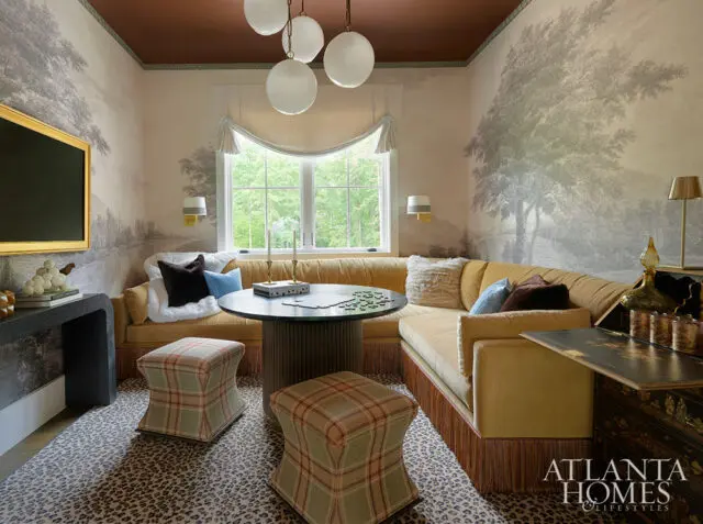 Yellow sectional sofa with fringe, plaid ottomans, and landscape wallpaper.