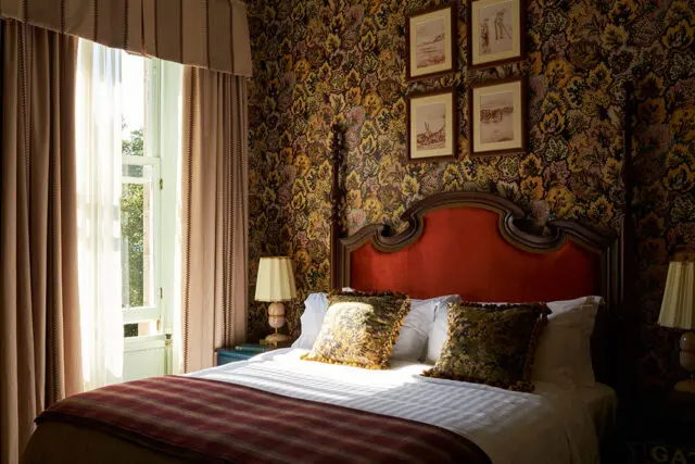 Guestroom with red upholstered headboard, patterned wallpaper, and striped curtains.