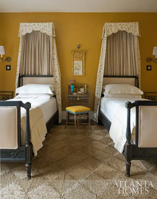 Bedroom with two twin beds, mustard yellow walls, and patterned canopy drapes.