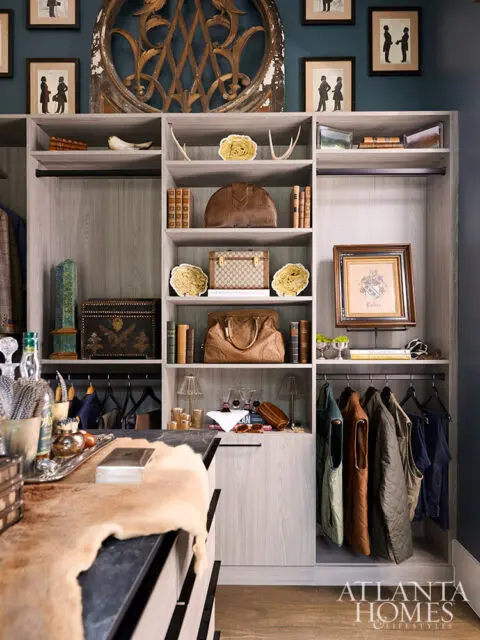 Walk-in closet with light wood shelves, leather bags, and framed art.