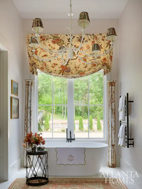 Freestanding bathtub with floral roman shade and chandelier. Atlanta Homes logo visible.