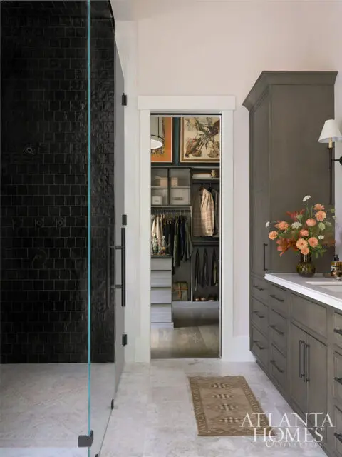 Walk-in closet with gray cabinetry and clothing, adjacent to a bathroom with a black tiled shower
