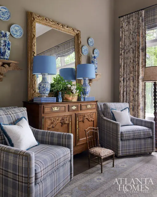 Living room with plaid armchairs, antique wooden cabinet, blue lamps, and ornate mirror.