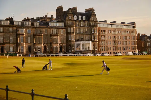 The Rusacks Hotel overlooks a golf course with golfers and golf carts.