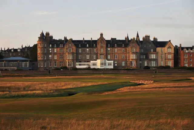 Stone building with multiple stories and varied architectural details, overlooking a golf course.