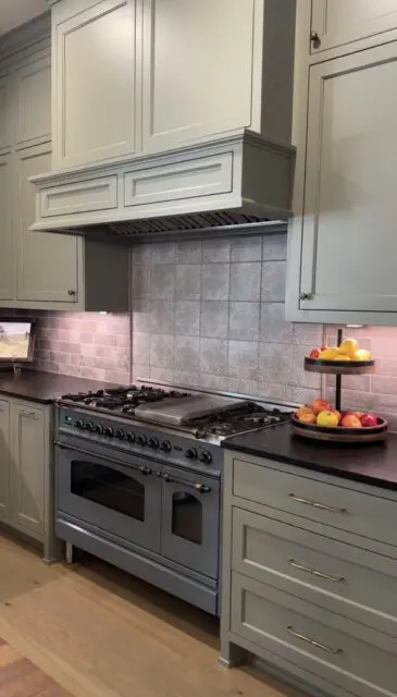 Gray kitchen with gray cabinets, stainless steel range, and patterned tile backsplash.