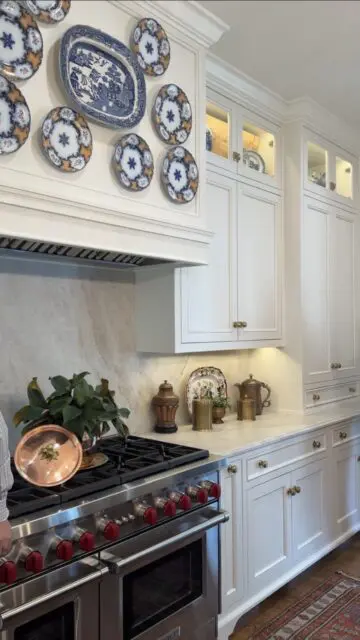 White kitchen with decorative plates on wall, marble backsplash, and stainless steel range.