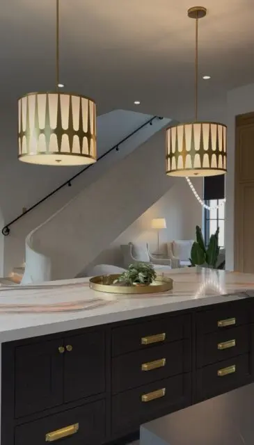 Kitchen island with black cabinets and marble countertop, two drum pendant lights above