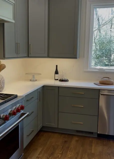 Gray kitchen cabinets with brass hardware, white quartz countertops, and a stainless steel range.