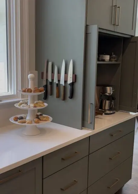 Green kitchen with white countertop, knife magnetic strip, tiered pastry stand, and open appliance