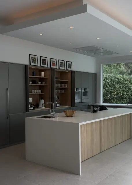 Modern kitchen with gray cabinets, wood-paneled island, and white countertop with sink.
