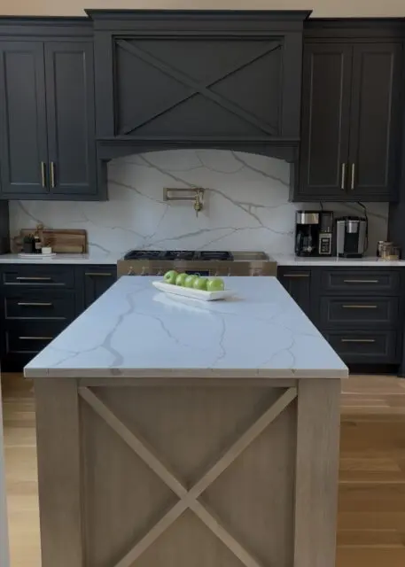 Dark gray kitchen cabinets with brass hardware, white quartz island, and wood island base