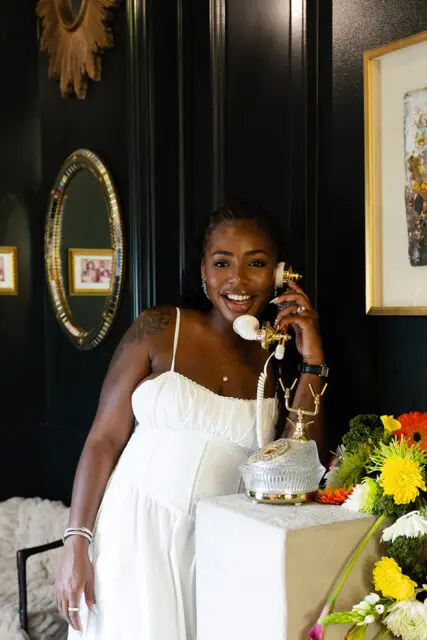 Woman in white dress holding vintage telephone, dark green walls, ornate mirror