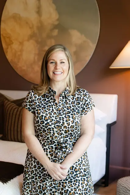 Woman in leopard print dress smiling in bedroom with large circular art
