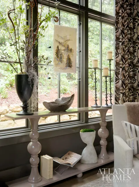 Console table with urn, bowl, and artwork by window; Atlanta Homes & Lifestyles logo