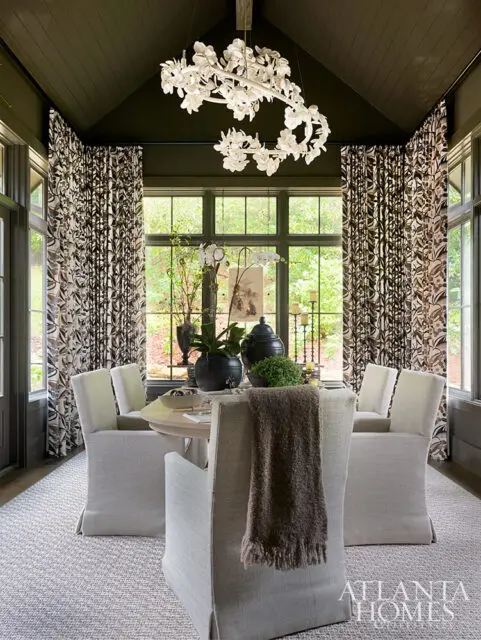 Dining room with floral curtains, light upholstered chairs, and a white floral chandelier.