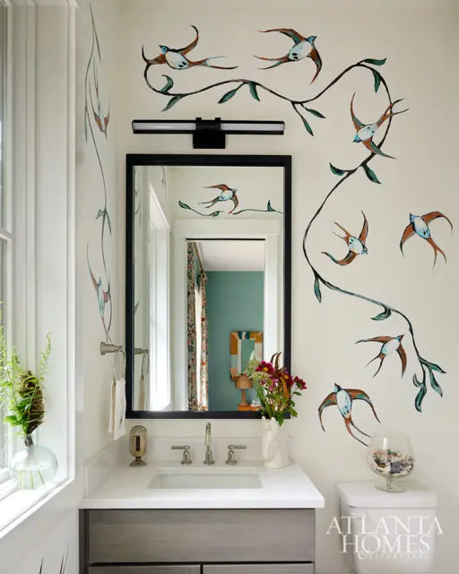 Bathroom with bird and branch wallpaper, vanity with white countertop, and black framed mirror.