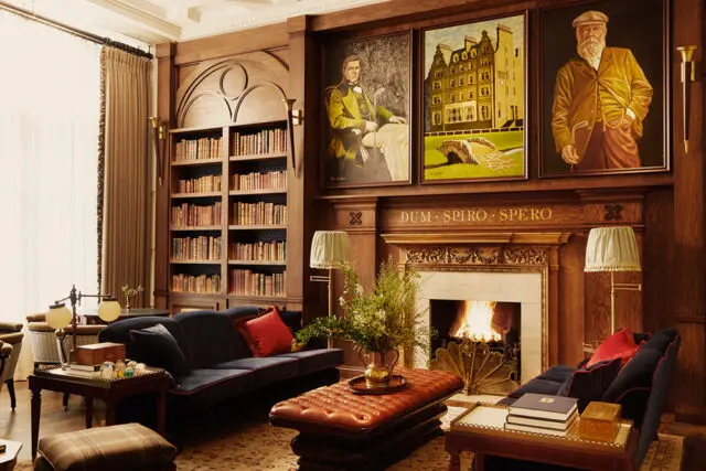 Library with dark wood paneling, built-in bookshelves, fireplace, and navy sofas.