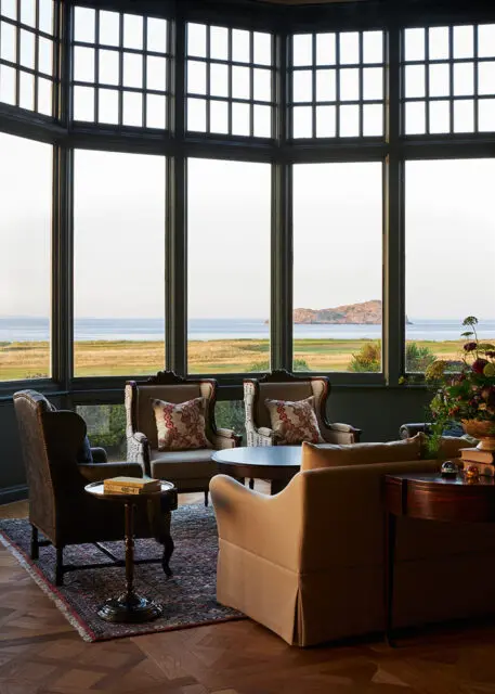 Lounge with wingback chairs, patterned pillows, and a bay window overlooking the sea