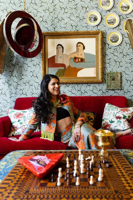 Woman in patterned outfit on red sofa, with framed art and decorative plates on wall.
