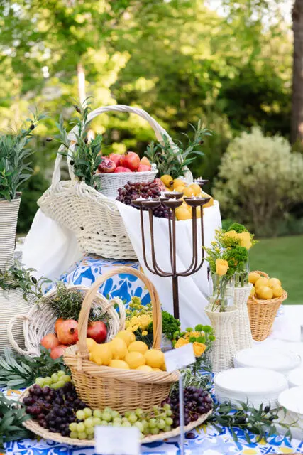 Outdoor fruit display with lemons, pomegranates, and grapes in wicker baskets.