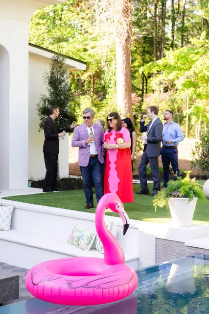 People mingling at an outdoor party by a pool with a pink flamingo float