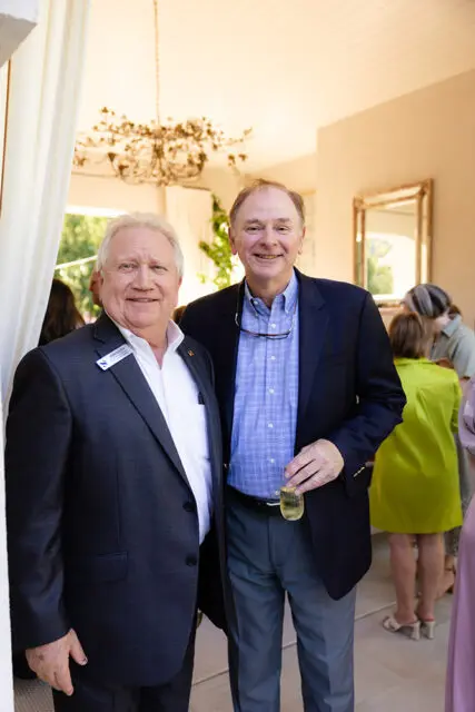 Two men in suits smiling, one holding a champagne flute.