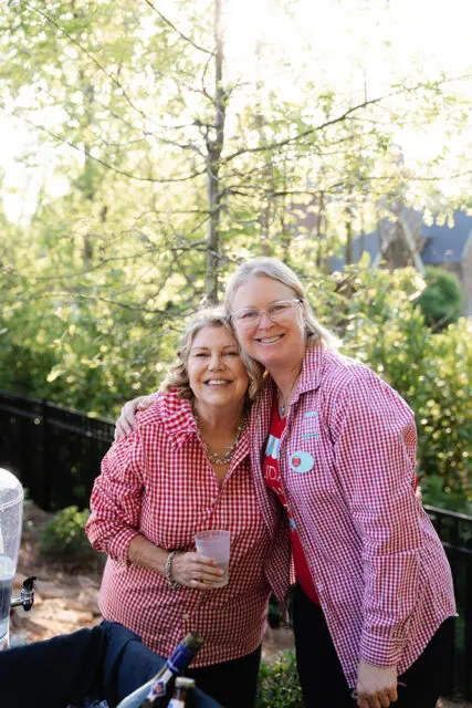 Two women in matching red gingham shirts smiling outdoors.