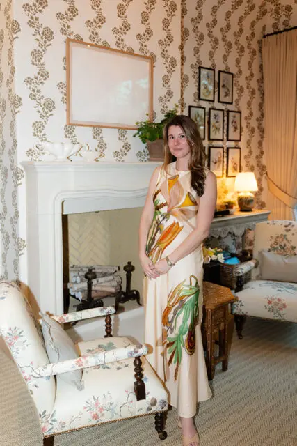 Woman in floral dress standing in a room with floral wallpaper and fireplace