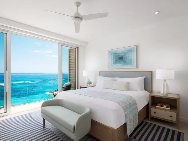 Bedroom with king bed, blue headboard, and ocean view through sliding glass doors.