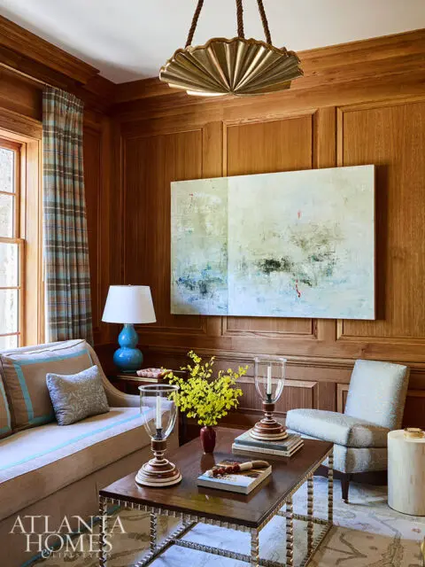 Living room with wood paneled walls, abstract art, and a sectional sofa.