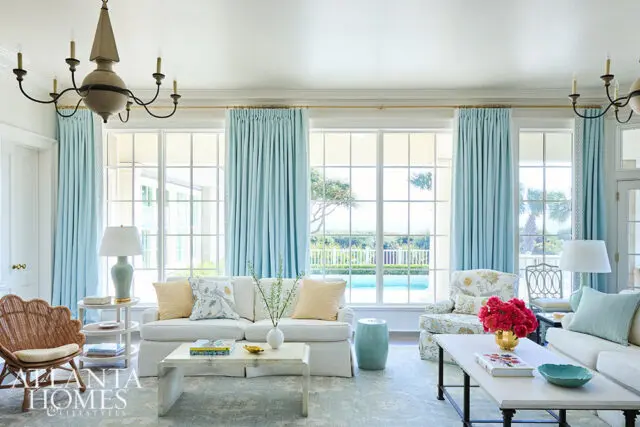 Living room with white sofas, light blue curtains, rattan chair, and pool view through large