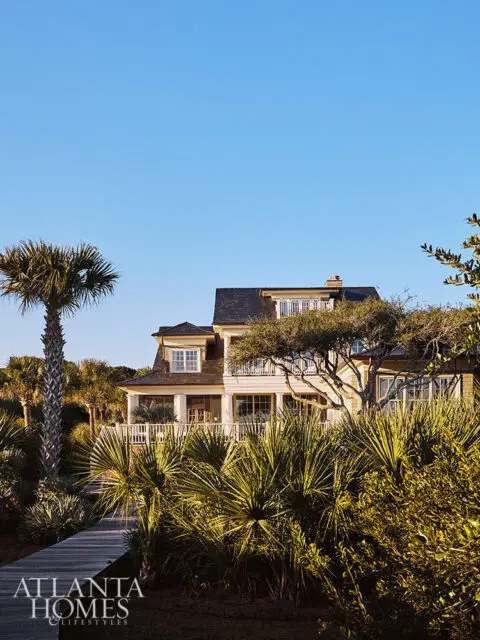 Coastal home with wrap-around porch surrounded by palm trees and lush vegetation.