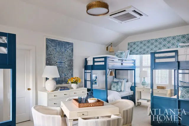 Blue bunk beds in a room with white walls, blue patterned art, and striped chairs.