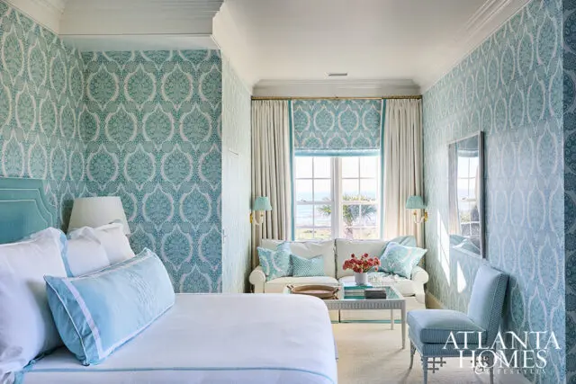 Bedroom with turquoise patterned wallpaper, white bedding, and a sofa facing a window with ocean