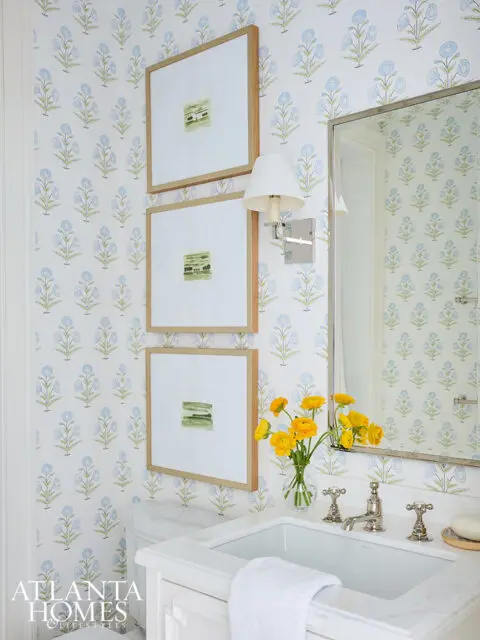 Powder room with blue floral wallpaper, three framed art pieces, and a white vanity with a marble
