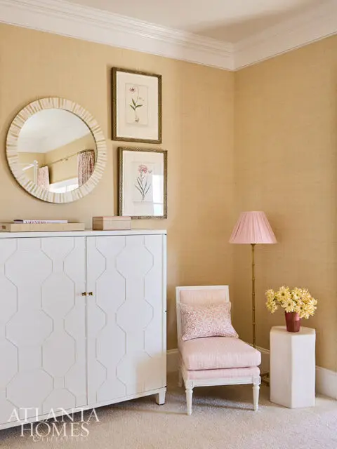 White cabinet with geometric pattern, pink upholstered chair, and botanical prints on textured