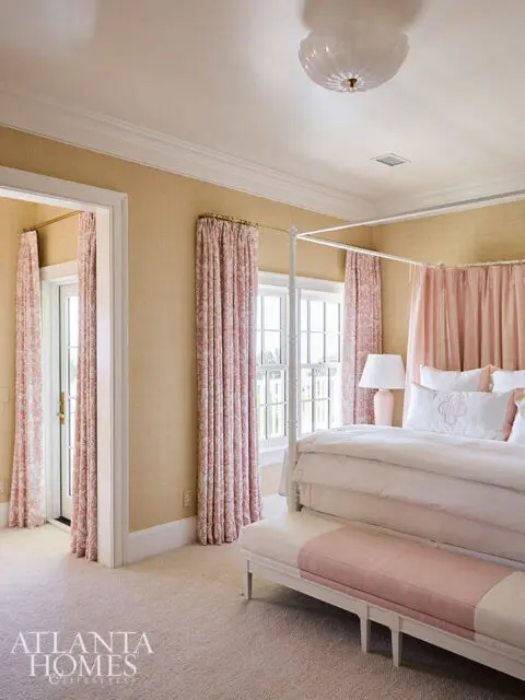 Bedroom with four-poster bed, pink floral curtains, and textured yellow wallpaper.