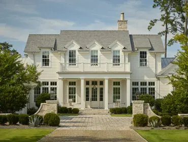 White clapboard house with gray shingle roof, dormer windows, and covered porch with columns.