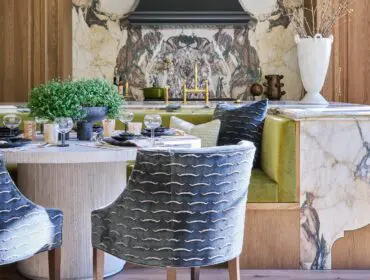 Marble-clad kitchen with a gold faucet and upholstered chairs.