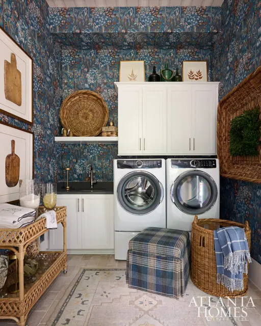 Laundry room with blue floral wallpaper, white cabinets, washer and dryer, and wicker accents.