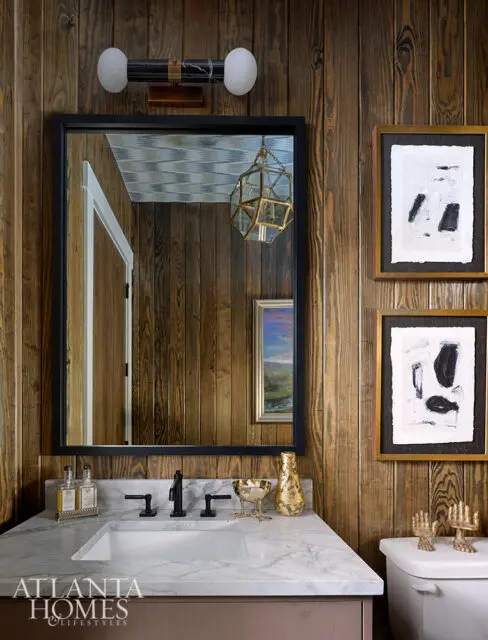 Wood-paneled bathroom with marble vanity, black faucet, and abstract art