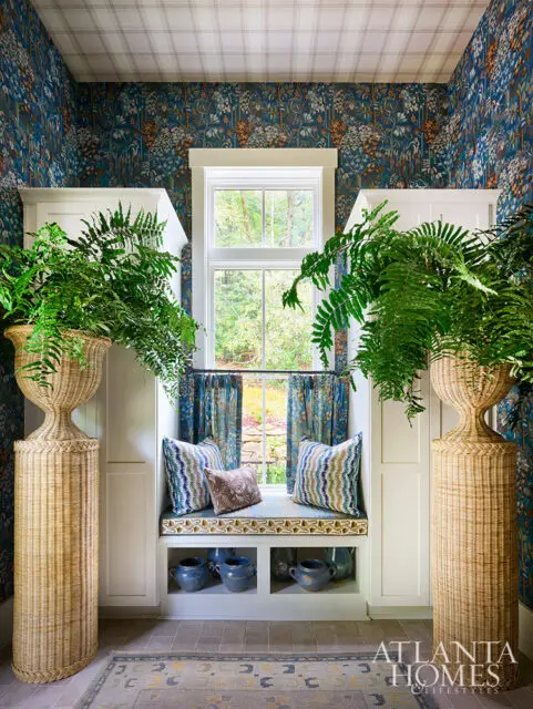Window seat with blue floral wallpaper, patterned pillows, and large woven planters.